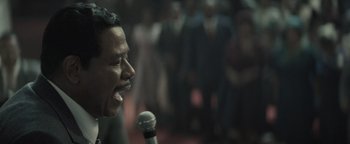 Movie still from “Respect” (2021), directed by Liesl Tommy – A person holding a microphone on a stage; Close Up shot, Over the shoulder angle