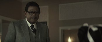 Movie still from “Respect” (2021), directed by Liesl Tommy – A man in a suit and tie standing in front of a fireplace; Close Up shot, Over the shoulder angle