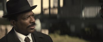 Movie still from “Respect” (2021), directed by Liesl Tommy – A man in a suit and a hat is looking to his left; Close Up shot, Over the shoulder angle