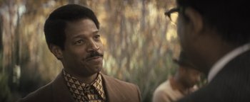 Movie still from “Respect” (2021), directed by Liesl Tommy – A man in a suit and tie looking at the camera; Close Up shot, Over the shoulder angle