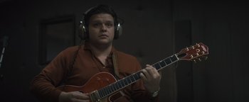 Movie still from “Respect” (2021), directed by Liesl Tommy – A man wearing headphones and holding a guitar; Close Up shot, High angle
