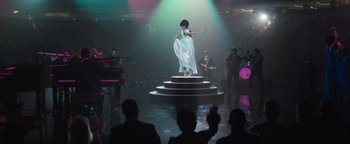 Movie still from “Respect” (2021), directed by Liesl Tommy – A woman standing on top of a stage in front of a crowd of onlookers; Extreme Wide shot, High angle