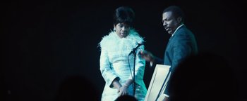 Movie still from “Respect” (2021), directed by Liesl Tommy – A man and a woman standing next to a microphone; Medium shot, Low angle