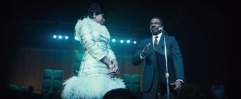 Movie still from “Respect” (2021), directed by Liesl Tommy – A man and a woman are holding hands in front of a microphone; Medium shot, Low angle