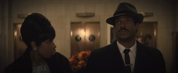 Movie still from “Respect” (2021), directed by Liesl Tommy – A man in a suit and a hat standing next to a woman in a black suit; Close Up shot, Low angle
