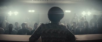 Movie still from “Respect” (2021), directed by Liesl Tommy – A woman is sitting in front of a group of people; Medium shot, Low angle