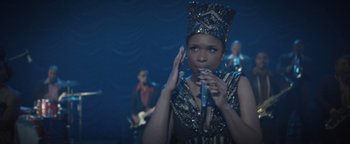 Movie still from “Respect” (2021), directed by Liesl Tommy – A woman holding a microphone in front of a band; Close Up shot, Over the shoulder angle