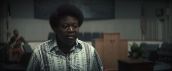 Movie still from “Respect” (2021), directed by Liesl Tommy – A man with a beard and a striped shirt is standing in a room; Close Up shot, Over the shoulder angle