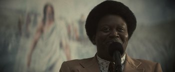 Movie still from “Respect” (2021), directed by Liesl Tommy – A man in a brown jacket is speaking into a microphone; Close Up shot, Over the shoulder angle