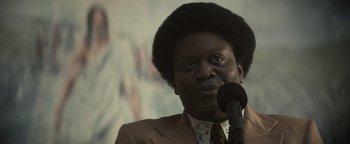 Movie still from “Respect” (2021), directed by Liesl Tommy – A man in a brown suit is speaking into a microphone; Close Up shot, Over the shoulder angle