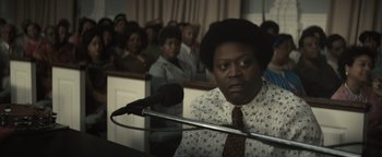 Movie still from “Respect” (2021), directed by Liesl Tommy – A man with a microphone in front of a group of people in a room; Close Up shot, Over the shoulder angle