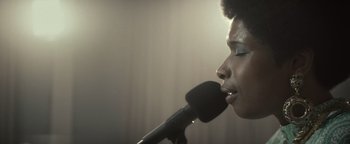 Movie still from “Respect” (2021), directed by Liesl Tommy – A person holding a microphone up to their mouth; Close Up shot, Low angle