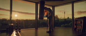 Movie still from “Retribution” (2023), directed by Nimród Antal – A man is standing in front of a large window and punching a punching bag; Wide shot, Low angle