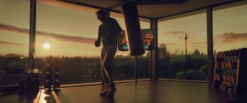 Movie still from “Retribution” (2023), directed by Nimród Antal – A man standing next to a punching bag in front of a large window; Wide shot, Low angle