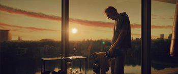 Movie still from “Retribution” (2023), directed by Nimród Antal – A man standing in front of a large window with a sunset in the background; Medium shot, Low angle