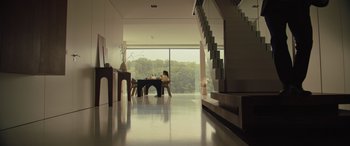 Movie still from “Retribution” (2023), directed by Nimród Antal – A person sitting at a table in a room with a large window; Wide shot, Low angle