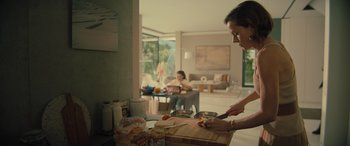 Movie still from “Retribution” (2023), directed by Nimród Antal – A woman cutting a sandwich on top of a wooden cutting board; Medium shot, Over the shoulder angle