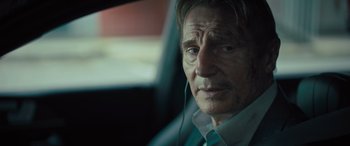 Movie still from “Retribution” (2023), directed by Nimród Antal – An older man wearing headphones while sitting in a car; Close Up shot, Over the shoulder angle