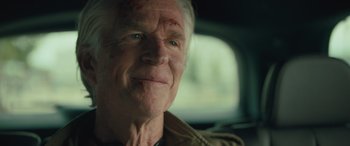 Movie still from “Retribution” (2023), directed by Nimród Antal – An older man with a scar on his face sitting in the back of a car; Close Up shot, Over the shoulder angle