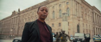 Movie still from “Retribution” (2023), directed by Nimród Antal – An older woman in a black jacket stands in front of a building; Medium shot, Low angle