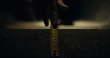 Movie still from “Barbarian” (2022), directed by Zach Cregger – A hand is pointing to a ruler on a piece of wood; Extreme Close Up shot, Low angle