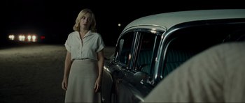 Movie still from “Revolutionary Road” (2008), directed by Sam Mendes – A woman standing in front of an old car at night; Medium shot, Over the shoulder angle