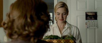 Movie still from “Revolutionary Road” (2008), directed by Sam Mendes – A woman is smiling while holding a basket of plants; Close Up shot, Over the shoulder angle