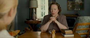 Movie still from “Revolutionary Road” (2008), directed by Sam Mendes – An older woman sitting at a table in a living room; Medium shot, Over the shoulder angle