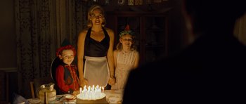 Movie still from “Revolutionary Road” (2008), directed by Sam Mendes – A woman standing next to a child in front of a cake; Medium shot, Over the shoulder angle