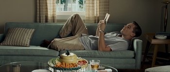 Movie still from “Revolutionary Road” (2008), directed by Sam Mendes – A man laying on a couch reading a book; Medium shot, Low angle