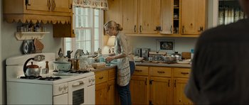 Movie still from “Revolutionary Road” (2008), directed by Sam Mendes – A woman standing in a kitchen washing dishes; Wide shot, Over the shoulder angle