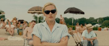 Movie still from “Revolutionary Road” (2008), directed by Sam Mendes – A woman wearing sunglasses standing in front of a group of people on a beach; Medium shot, Over the shoulder angle
