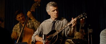 Movie still from “Revolutionary Road” (2008), directed by Sam Mendes – A man holding a guitar while standing next to a microphone; Medium shot, Low angle