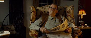 Movie still from “Revolutionary Road” (2008), directed by Sam Mendes – An older man sitting in a chair reading a newspaper; Medium shot, Over the shoulder angle