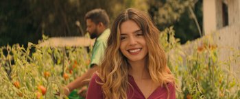 Movie still from “Rich in Love 2” (2023), directed by Bruno Garotti – A woman with long brown hair smiles for the camera; Close Up shot, Over the shoulder angle
