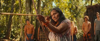 An older woman is holding a bow and arrow in the woods