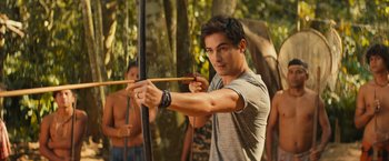 Movie still from “Rich in Love 2” (2023), directed by Bruno Garotti – A young man holding a bow and arrow in the woods; Medium shot, Over the shoulder angle