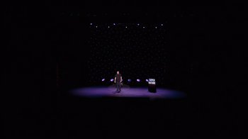 Movie still from “Ricky Gervais: SuperNature” (2022), directed by John L. Spencer – A man standing on a stage in front of a microphone; Extreme Wide shot, High angle