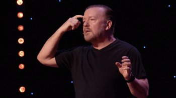 Movie still from “Ricky Gervais: SuperNature” (2022), directed by John L. Spencer – A man in a black t - shirt talking on a cell phone; Close Up shot, High angle