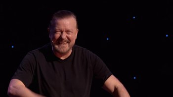Movie still from “Ricky Gervais: SuperNature” (2022), directed by John L. Spencer – A man with a beard is smiling for the camera; Close Up shot, High angle