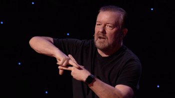 Movie still from “Ricky Gervais: SuperNature” (2022), directed by John L. Spencer – A man with a beard and a black t - shirt; Close Up shot, Overhead angle