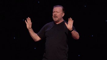 Movie still from “Ricky Gervais: SuperNature” (2022), directed by John L. Spencer – A man with a beard and a black t - shirt; Close Up shot, High angle