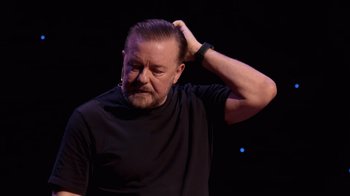 Movie still from “Ricky Gervais: SuperNature” (2022), directed by John L. Spencer – A person holding his head; Close Up shot, Over the shoulder angle