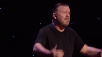 Movie still from “Ricky Gervais: SuperNature” (2022), directed by John L. Spencer – A man with a goatee and a black t - shirt; Medium shot, High angle