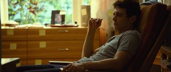 Movie still from “Rise of the Planet of the Apes” (2011), directed by Rupert Wyatt – A man sitting on a couch holding a cell phone; Medium shot, Over the shoulder angle