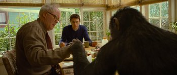 Movie still from “Rise of the Planet of the Apes” (2011), directed by Rupert Wyatt – A man sitting at a table with two other people; Medium shot, Over the shoulder angle