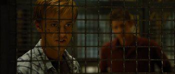 Movie still from “Rise of the Planet of the Apes” (2011), directed by Rupert Wyatt – A young man behind a metal fence looking at the camera; Close Up shot, Low angle