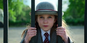 Movie still from “Roald Dahl's Matilda the Musical” (2022), directed by Matthew Warchus – A young girl in a hat and tie holding onto a fence; Close Up shot, Low angle