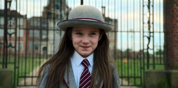 Movie still from “Roald Dahl's Matilda the Musical” (2022), directed by Matthew Warchus – A young girl wearing a suit and tie and wearing a hat; Close Up shot, Over the shoulder angle