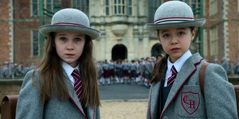 Movie still from “Roald Dahl's Matilda the Musical” (2022), directed by Matthew Warchus – Two young girls in school uniforms standing next to each other in front of a group of people; Close Up shot, High angle
